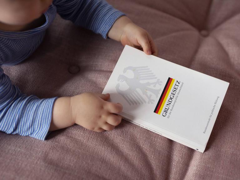 Ein Kleinkind hält ein deutsches Grundgesetz in der Hand.