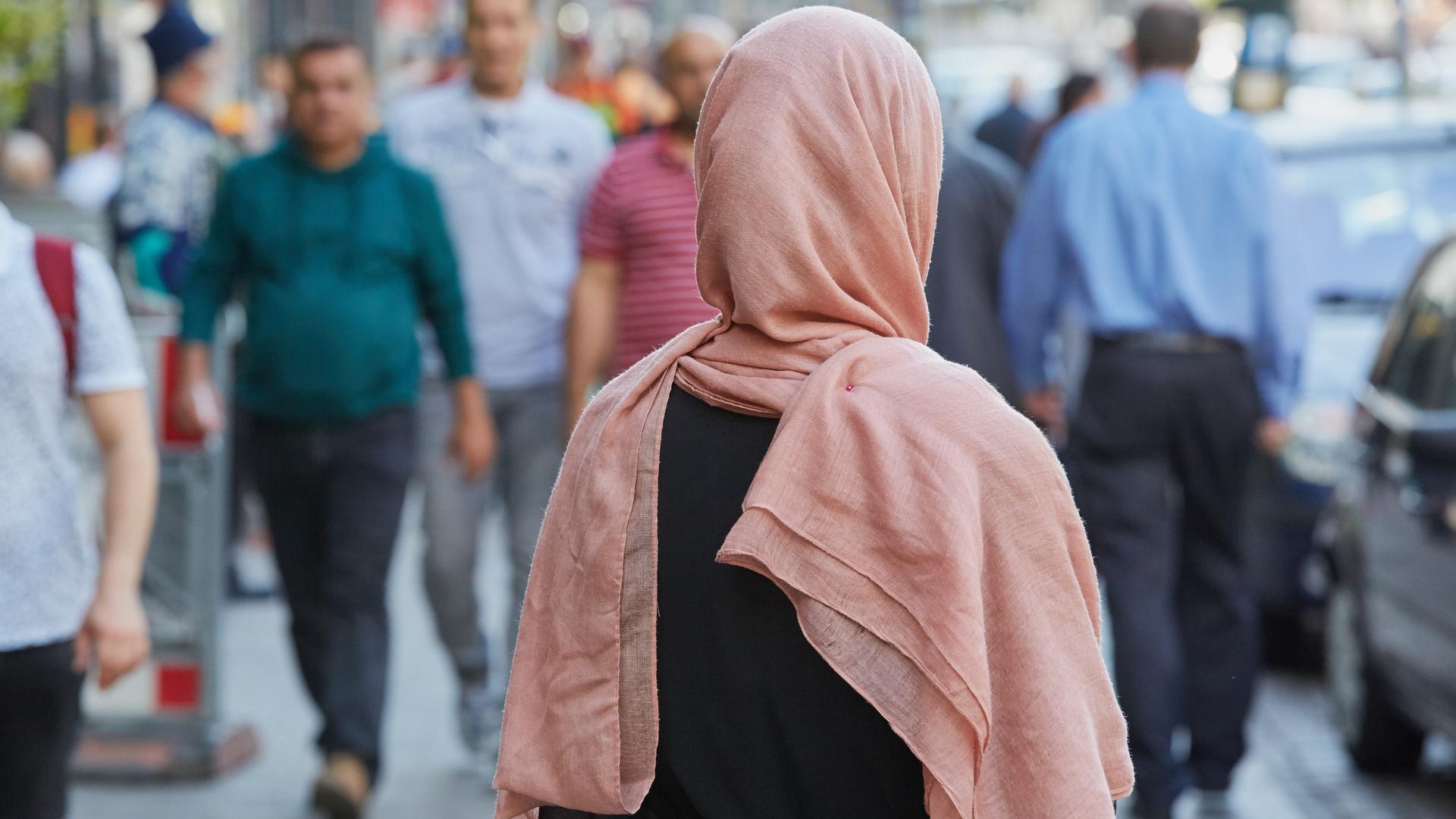 Eine Frau mit Kopf-Tuch steht auf einem Bürger-Steig. Sie wendet uns den Rücken zu. Eine Frau mit Kopf-Tuch steht auf einem Bürger-Steig. Sie wendet uns den Rücken zu.