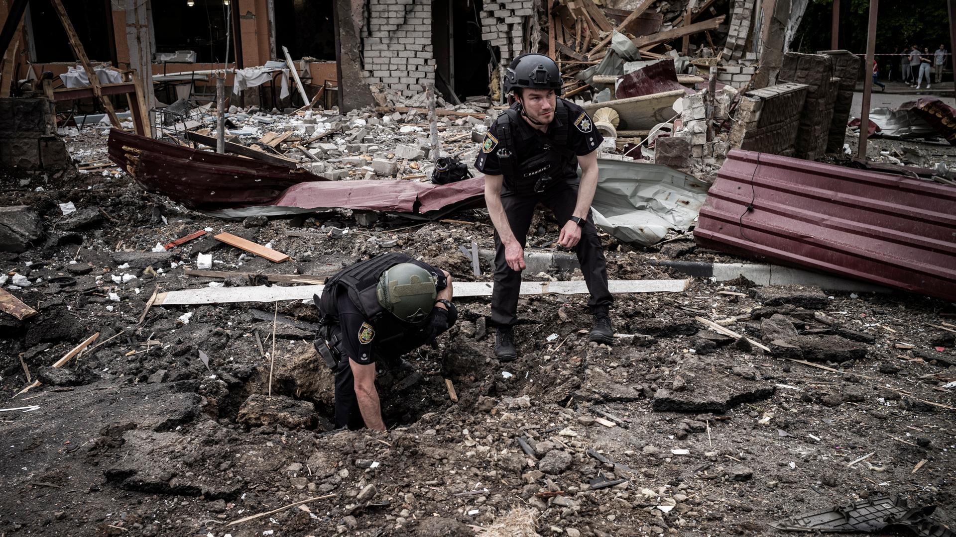 Soldaten inspizieren einen Bombenkrater zwischen Trümmern.