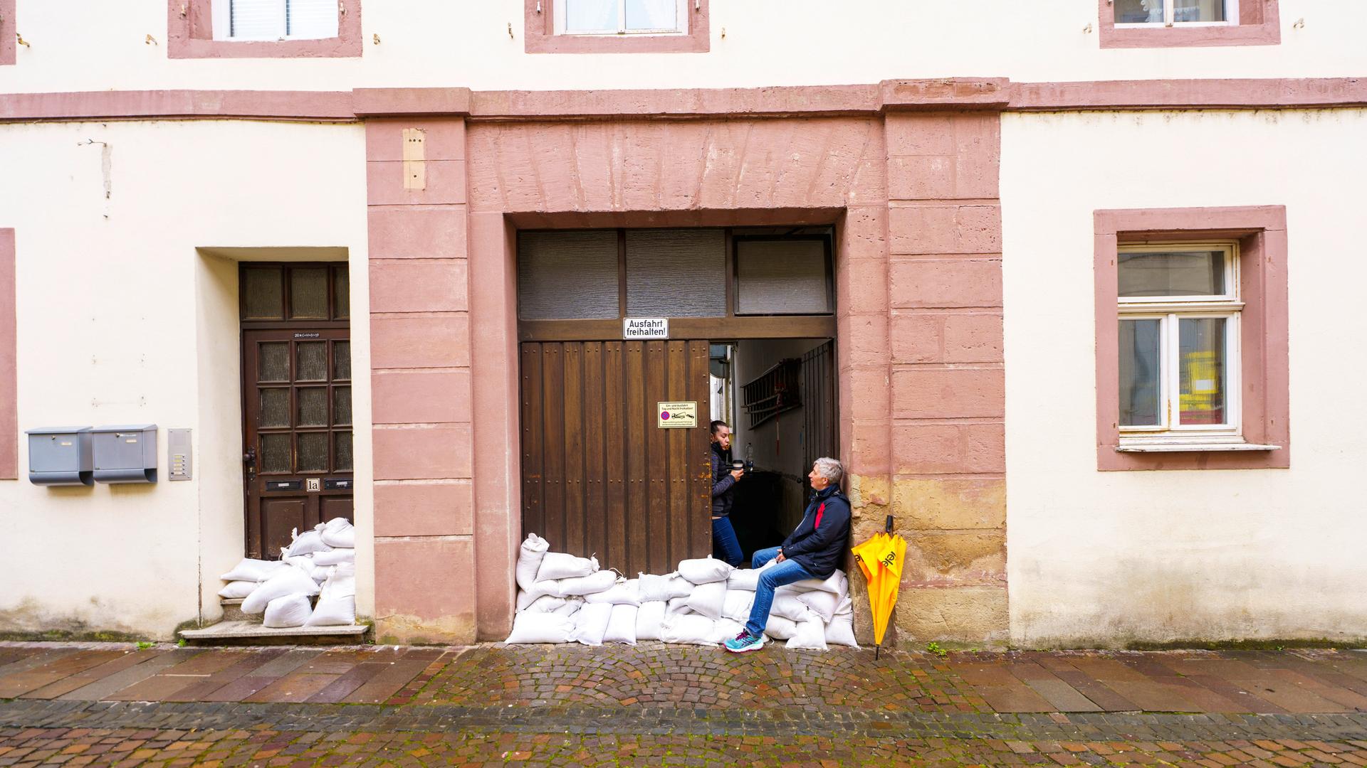 Die Bewohner einer Altstadt sind mit Abpumpen und Abräumen nach dem Hochwasser beschäftigt. Ein Mann sitzt auf Sandsäcken, mit denen der Eingang zu einem Haus gesichert wurde.