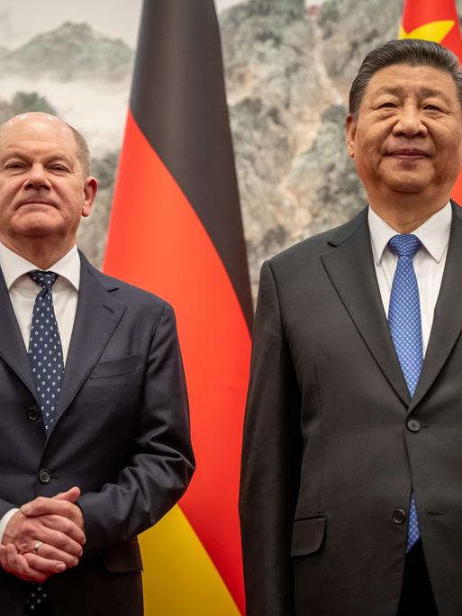 Bundeskanzler Olaf Scholz (SPD) und Chinas Staatspräsident von China, Xi Jinping, stehen vor deutschen und chinesischen Flaggen und blicken in die Kamera. 