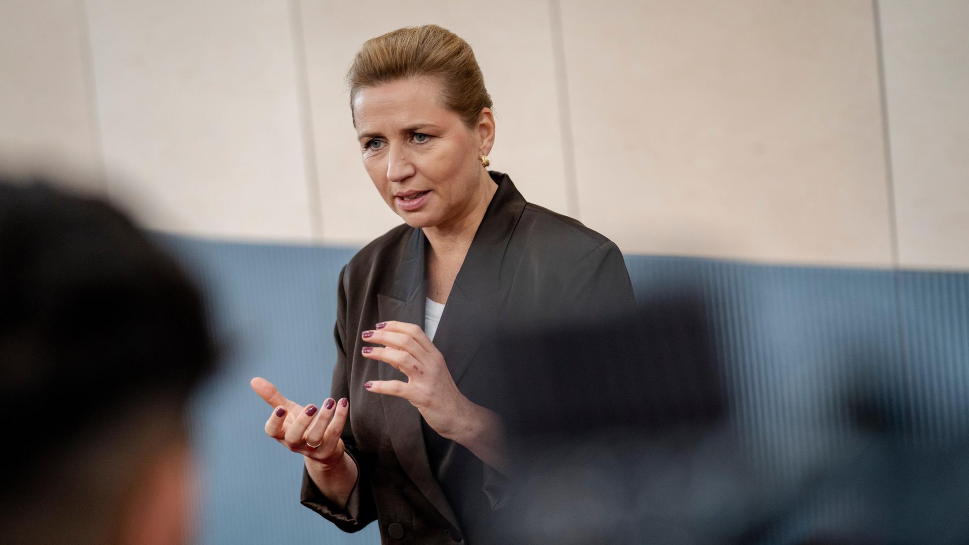 Dänemarks Ministerpräsidentin Mette Frederiksen steht vor einer Gruppe und spricht.  