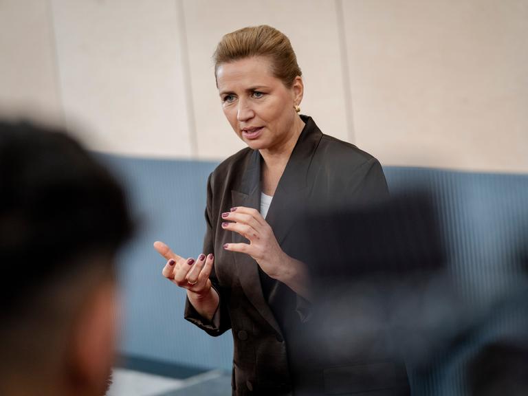 Dänemarks Ministerpräsidentin Mette Frederiksen steht vor einer Gruppe und spricht.  