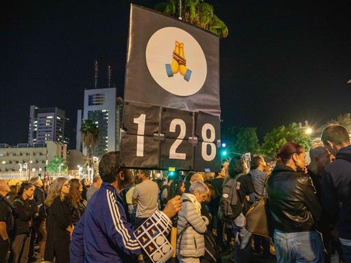 Zahlreiche Menschen sind in Tel Aviv bei einer Demonstration für einen Waffenstillstand, die Rückkehr der Geiseln und einen sofortigen Gefangenenaustausch zu sehen. Im Vordergrund ein Schild, das die Zahl 128 zeigt - die Zahl der Tage, welche die Geiseln in Gefangenschaft sind. 