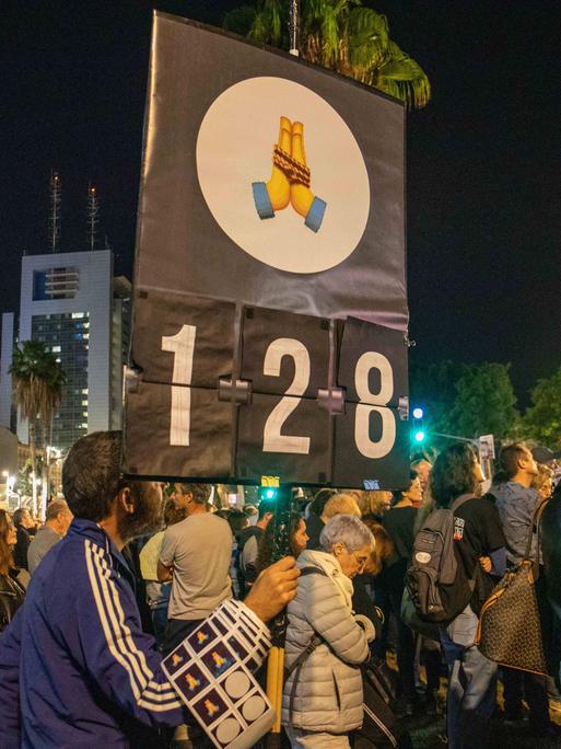 Zahlreiche Menschen sind in Tel Aviv bei einer Demonstration für einen Waffenstillstand, die Rückkehr der Geiseln und einen sofortigen Gefangenenaustausch zu sehen. Im Vordergrund ein Schild, das die Zahl 128 zeigt - die Zahl der Tage, welche die Geiseln in Gefangenschaft sind. 