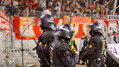 Polizisten in Montur stehen vor einer Fankurve in einem Fußballstadion.