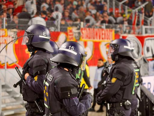 Polizisten in Montur stehen vor einer Fankurve in einem Fußballstadion.