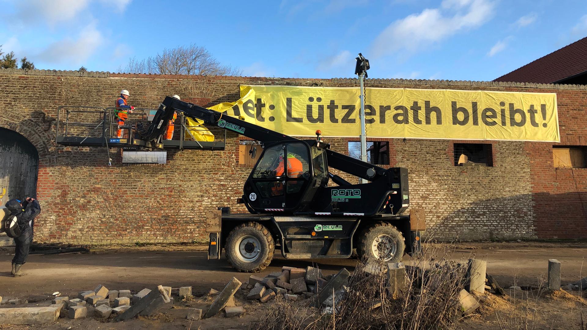 Arbeiter entfernen ein Banner "Lützerath bleibt!" von einer Wand. 