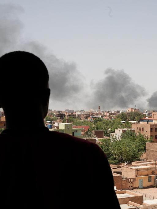 Rauch über Häusern in der sudanesischen Hauptstadt Khartum. Ein Mann steht im Vordergrund, er ist nur eine Silhouette.