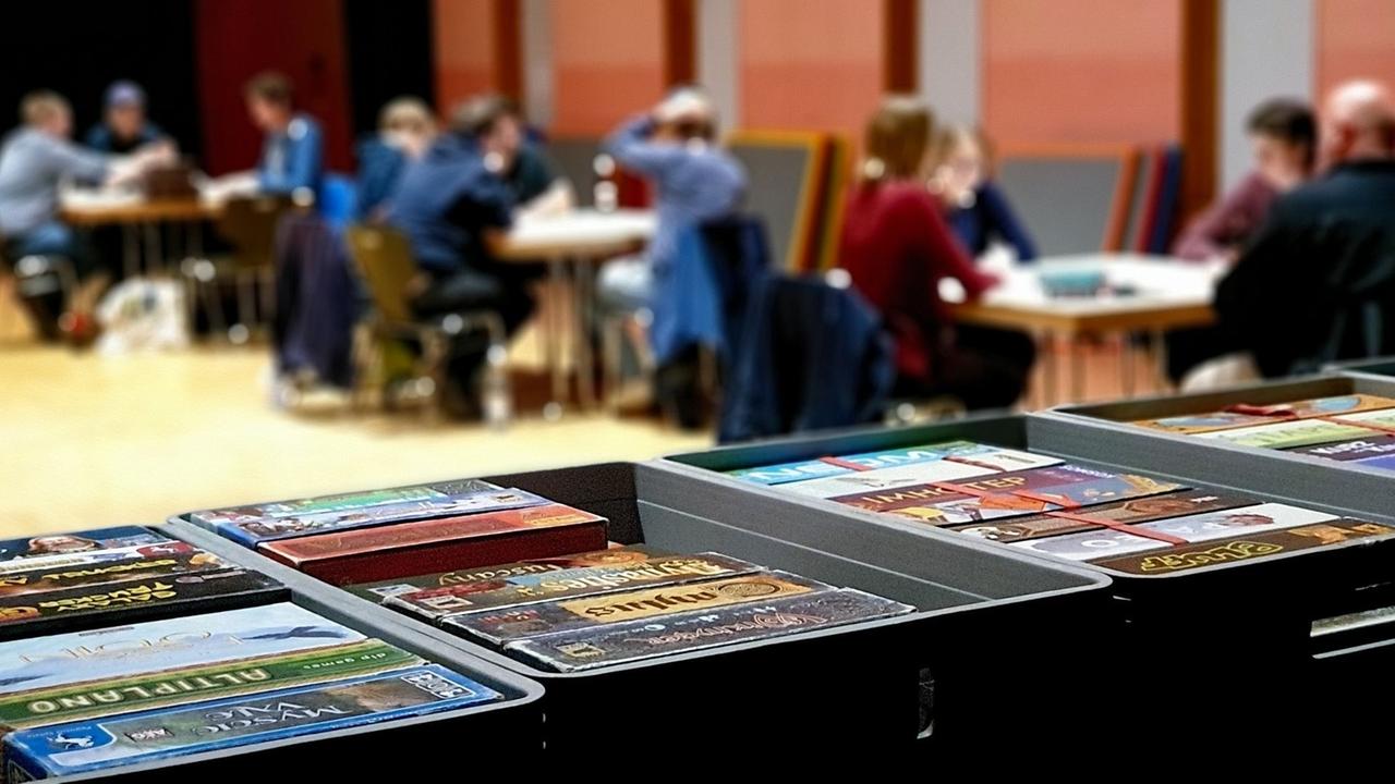 Im Vordergrund sind Spielkartenstapel zu sehen, während im Hintergrund an drei Tischen gespielt wird.