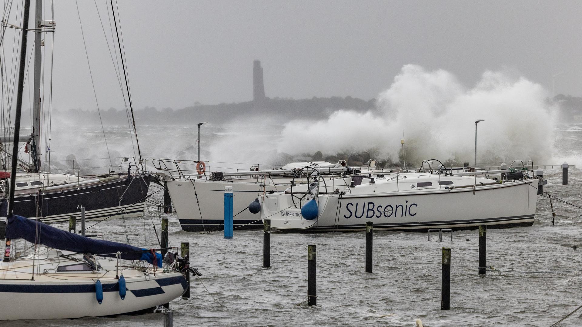 Meterhohe Wellen brechen sich an der Hafenanlagen in Schilksee. Im Hafen liegen mehrere Segelboote. Meterhohe Wellen brechen sich an der Hafenanlagen in Schilksee. Im Hafen liegen mehrere Segelboote.