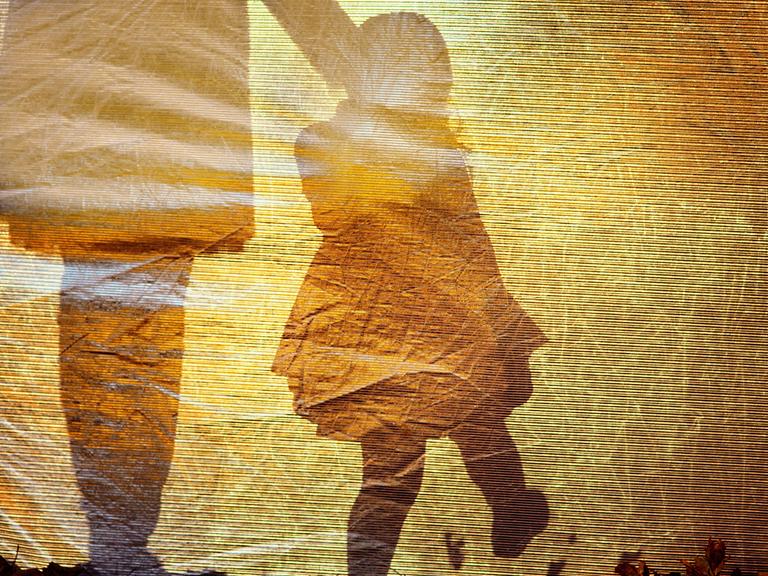 Schatten eines Erwachsenen und eines Kindes auf einem goldorangefarbenen Untergrund.