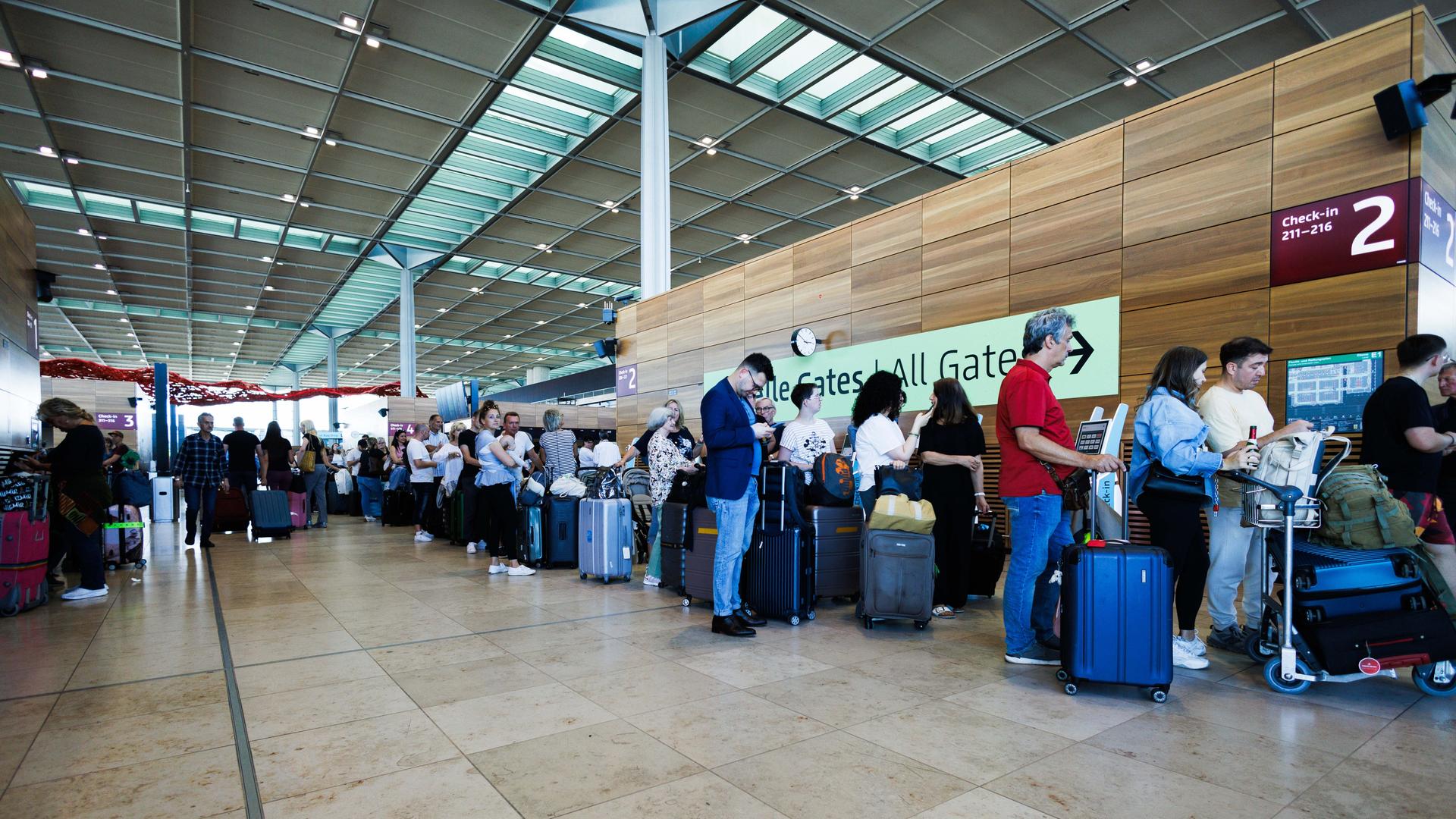 Am Berliner Flughafen stehen Menschen mitihren Koffern in einer sehr langen Schlange. 