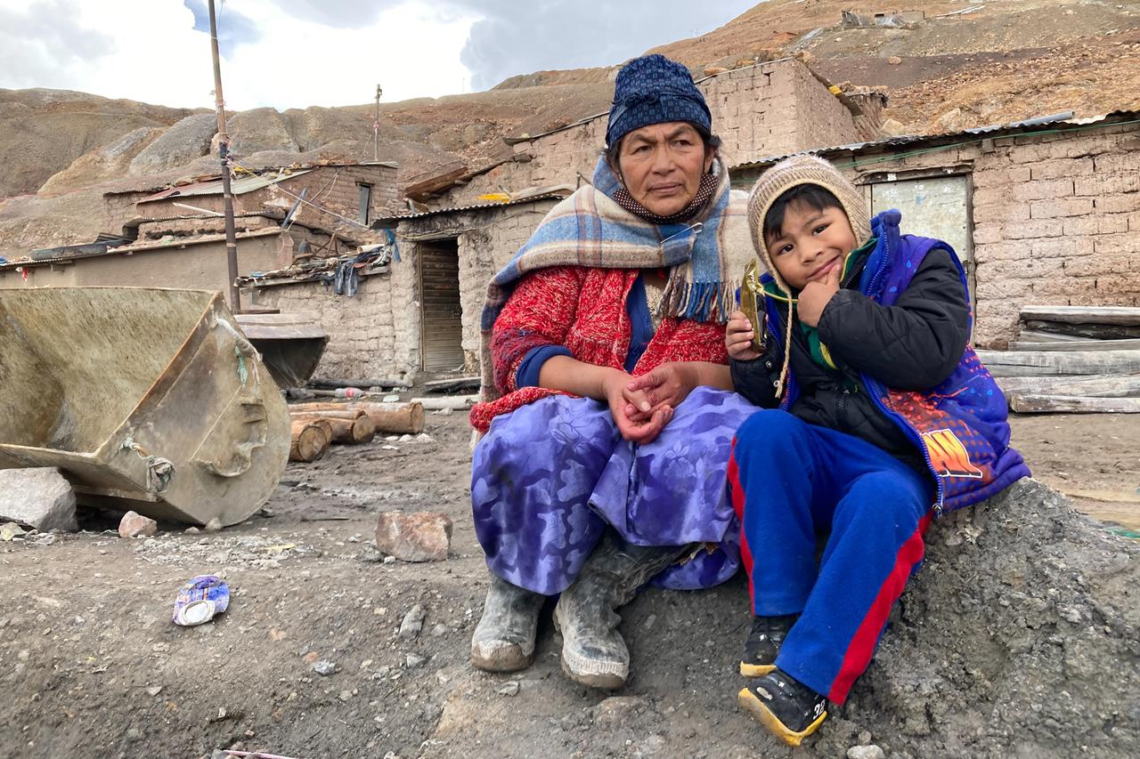 Eine Frau und ein kleiner Junge sitzen auf kargem Boden vor ärmlichen Steinhütten