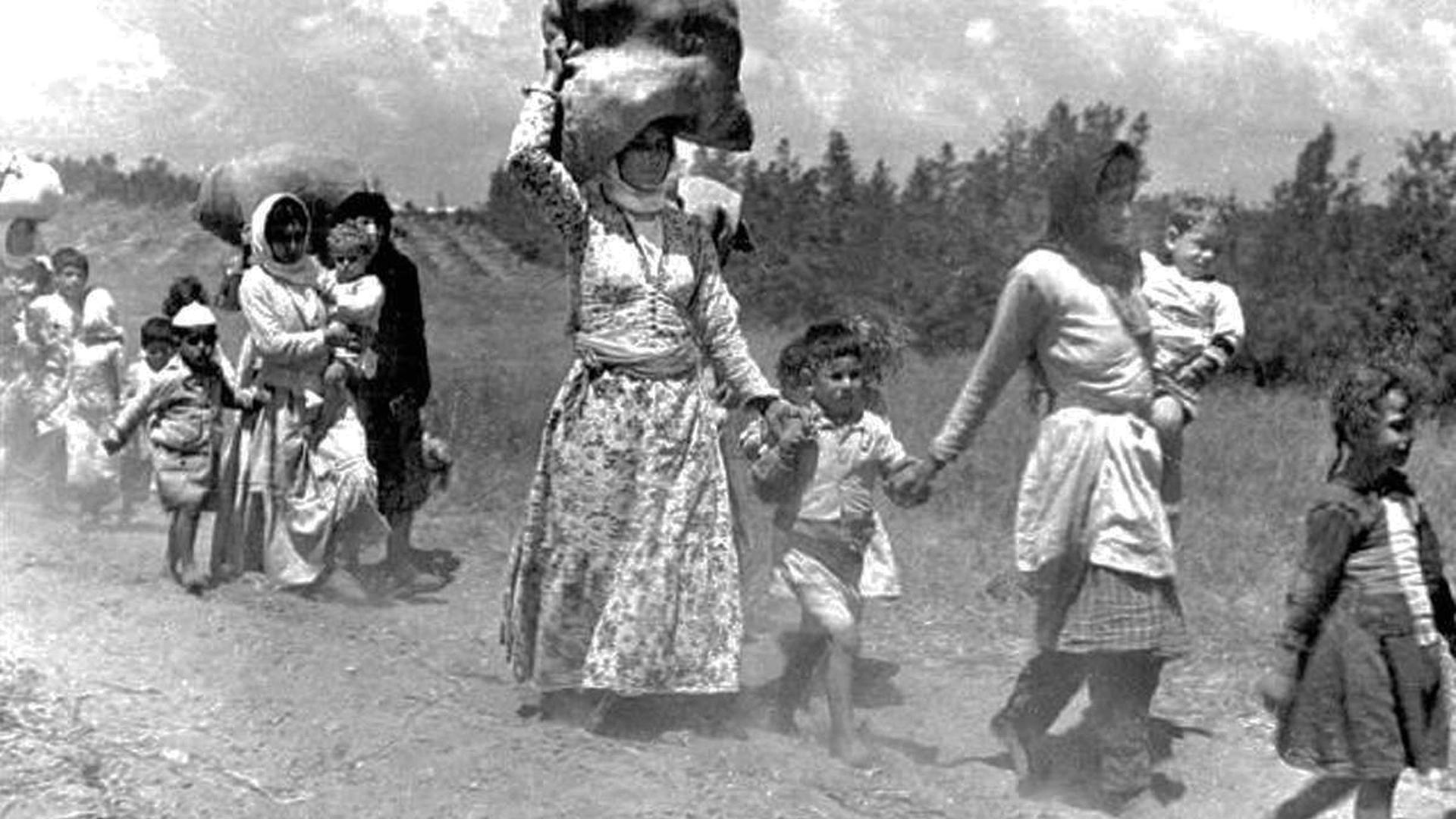 1948: Palästinensische Frauen und Kinder auf der Flucht. Eine Fraut trägt einen großen Sack auf ihrem Kopf.