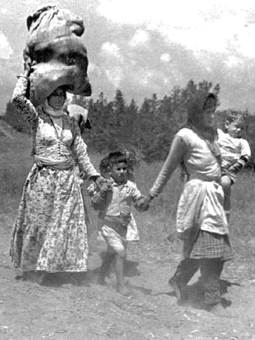 1948: Palästinensische Frauen und Kinder auf der Flucht. Eine Fraut trägt einen großen Sack auf ihrem Kopf.
