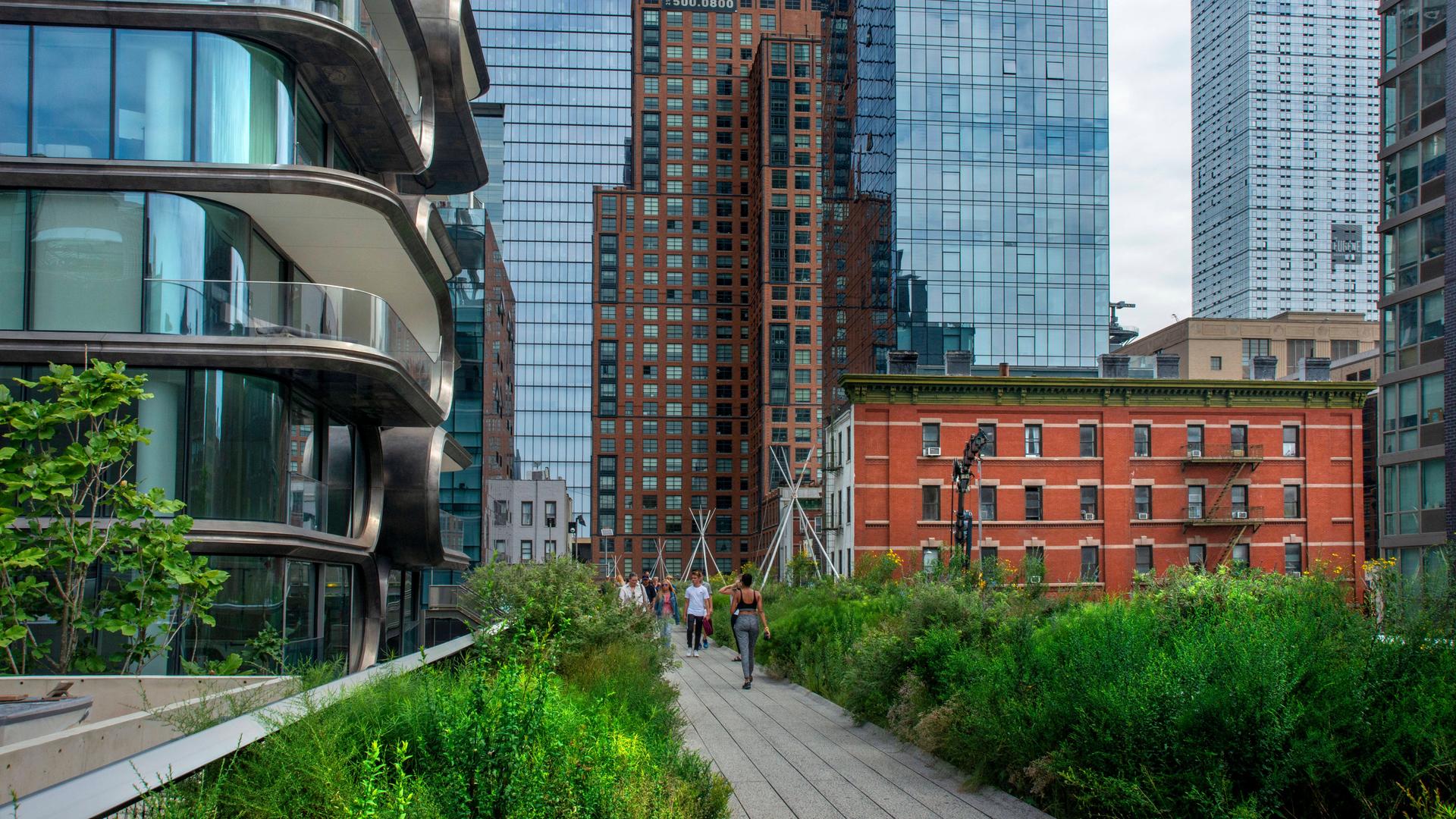 Der grüne Highline Park in Manhattan ist von Häusern umgeben, im Hintergrund sieht man zwei Wolkenkratzer. Der grüne Highline Park in Manhattan ist von Häusern umgeben, im Hintergrund sieht man zwei Wolkenkratzer.