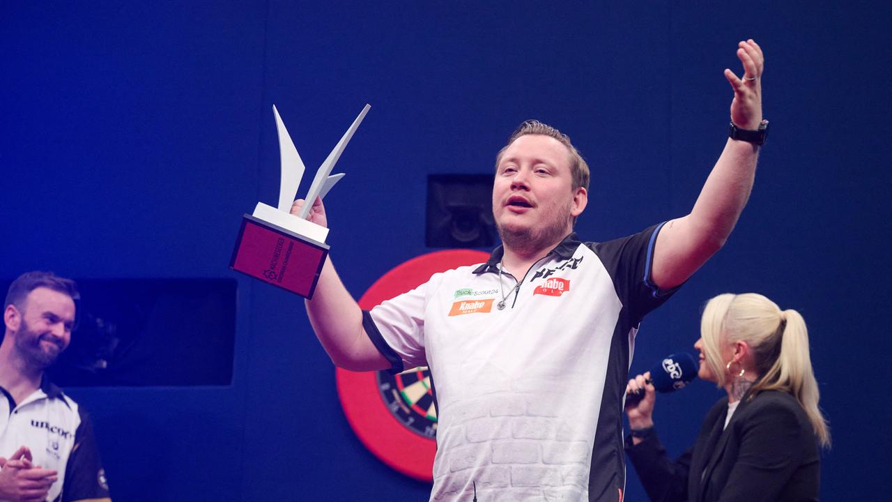 Martin Schindler hält in einer Hand die Trophäe für den zweiten Platz bei der Darts-Europameisterschaft. Die andere Hand hat er hoch erhoben. 