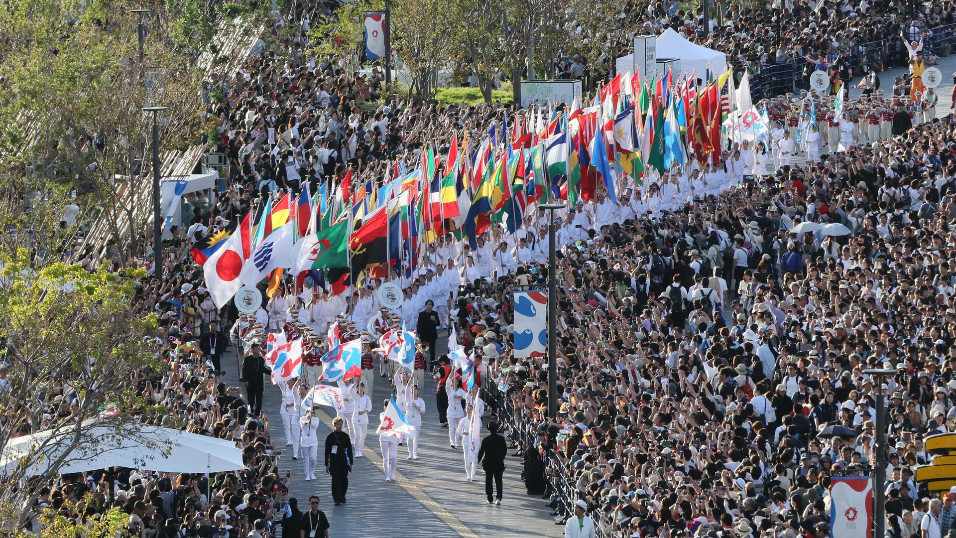 In einer Parade ziehen die Teilnehmer der Expo 2025 mit den Landesfahnen durch tausende Zuschauer.
