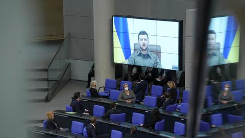 Im Bundestag ist eine große Videoleinwand, von der der ukrainische Präsident Wolodymyr Selenskyj spricht. Abgeordnete haben sich zu ihm umgedeht.