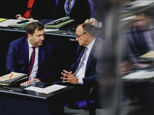 SPD-Chef und Finanzminister Lars Klingbeil (SPD) und Kanzler Friedrich Merz (CDU) sitzen im Bundestag nebeneinander und führen ein ernstes Gespräch. Der Kanzler verzieht dabei das Gesicht. SPD-Chef und Finanzminister Lars Klingbeil (SPD) und Kanzler Friedrich Merz (CDU) sitzen im Bundestag nebeneinander und führen ein ernstes Gespräch. Der Kanzler verzieht dabei das Gesicht.