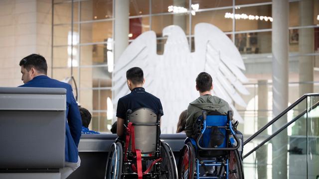 Zwei junge Menschen im Roll-stuhl sitzen auf der Besucher-Tribüne im Bundestag.