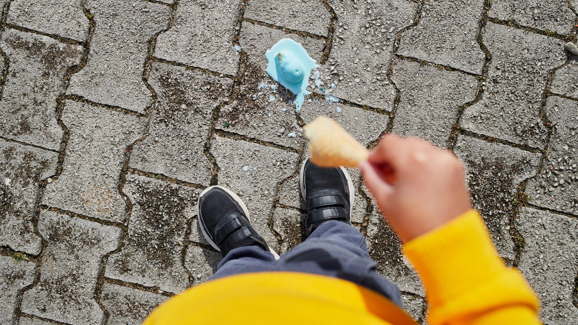 Blick vor die Füße einer Person. Dort liegt eine schmelzende Eiskugel, die von der Waffel gefallen ist. Blick vor die Füße einer Person. Dort liegt eine schmelzende Eiskugel, die von der Waffel gefallen ist.