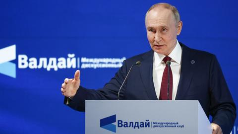 Putin steht an einem Redepult und spricht in ein Mikrofon.