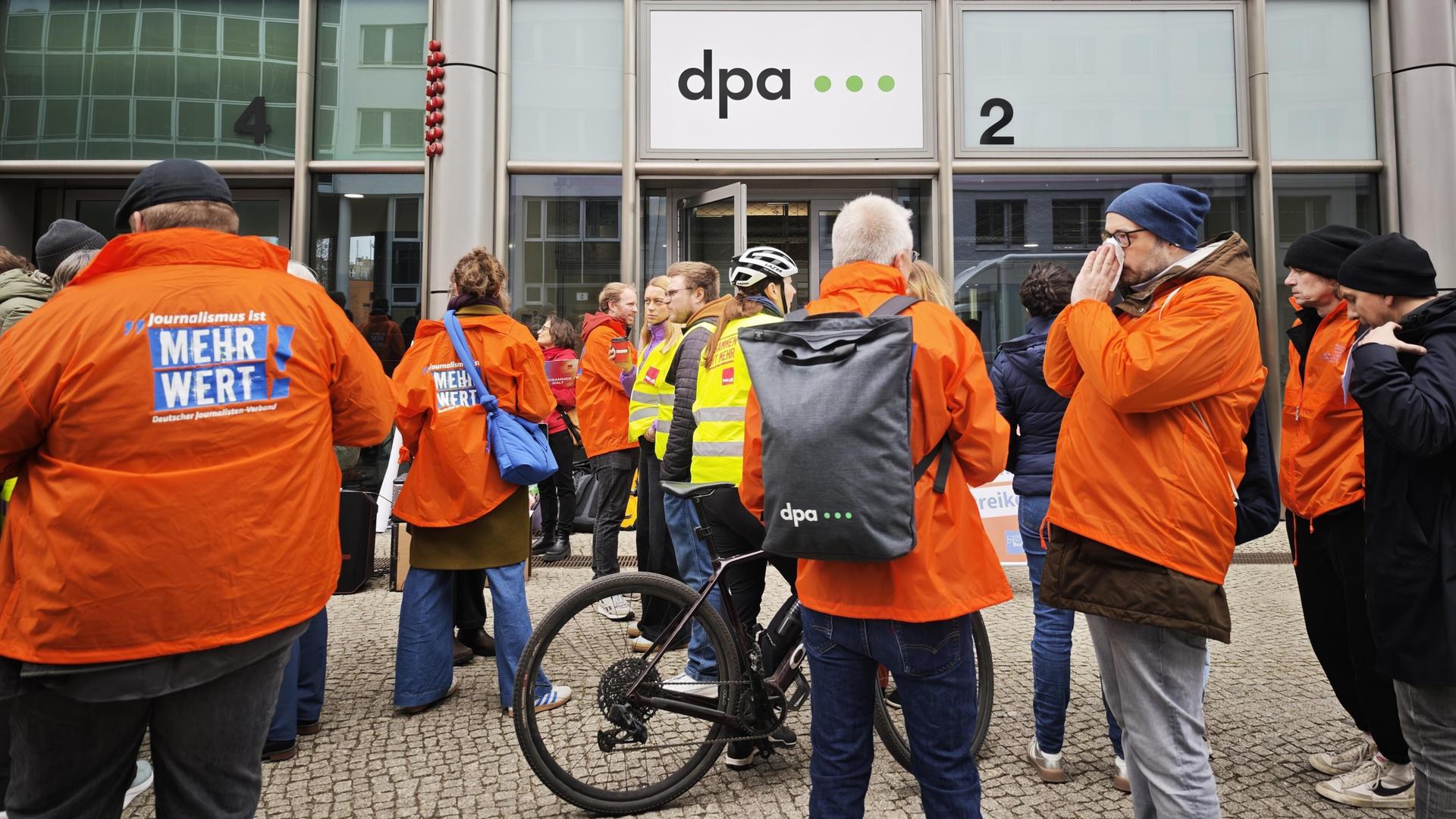 Verdi-Streik in der Zentrale der Nachrichtenagentur dpa; Mitarbeiter stehen in orangen Jacken vor dem Gebäude.