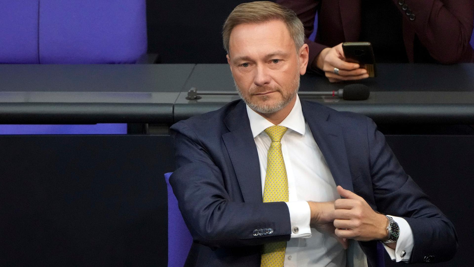 Bundesfinanzminister Lindner sitzt im Bundestag. Er greift sich mit der rechten Hand in die Innentasche der Jacke. Bundesfinanzminister Lindner sitzt im Bundestag. Er greift sich mit der rechten Hand in die Innentasche der Jacke.