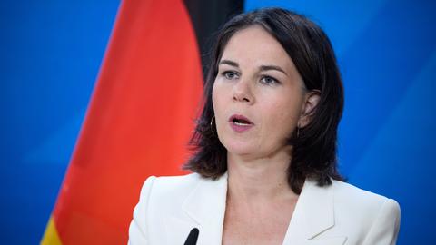 Außenministerin Annalena Baerbock (Bündnis 90/Die Grünen), in weißem Blazer spricht vor einem Mikrofon, im Hintergrund die deutsche Flagge.