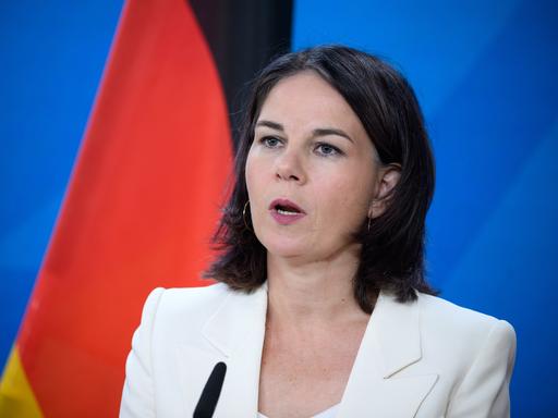 Außenministerin Annalena Baerbock (Bündnis 90/Die Grünen), in weißem Blazer spricht vor einem Mikrofon, im Hintergrund die deutsche Flagge.
