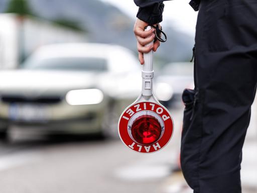 Ein Polizist steht am Straßenrand einer Autobahn und hält seine Kelle in der Hand.