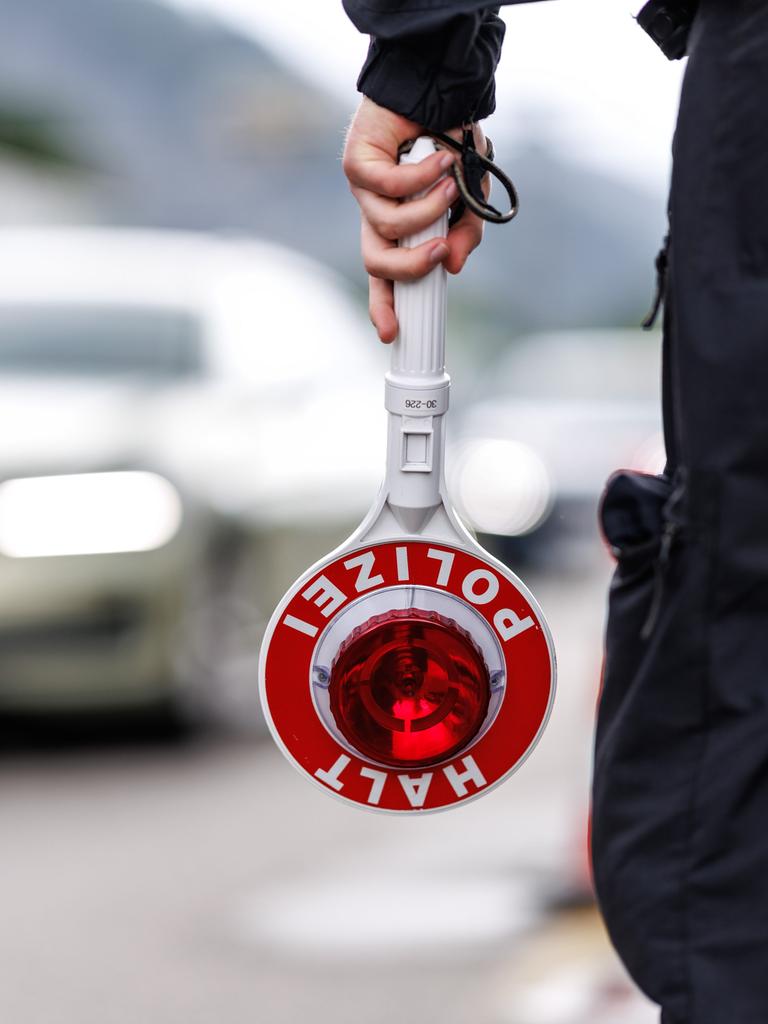 Ein Polizist steht am Straßenrand einer Autobahn und hält seine Kelle in der Hand.