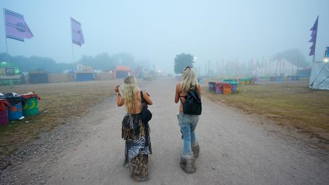 Zwei Besucherinnen sind von hinten zu sehen bei ihrem Weg zum Glastonbury-Festival 