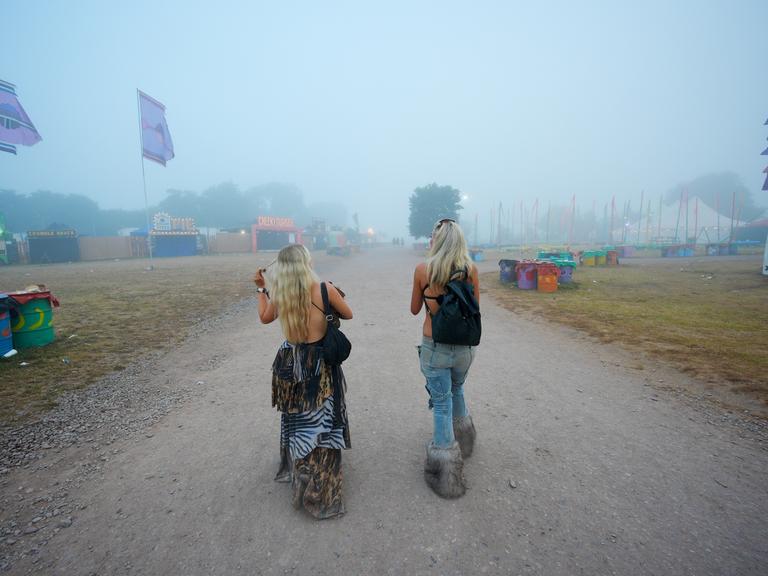 Zwei Besucherinnen sind von hinten zu sehen bei ihrem Weg zum Glastonbury-Festival 