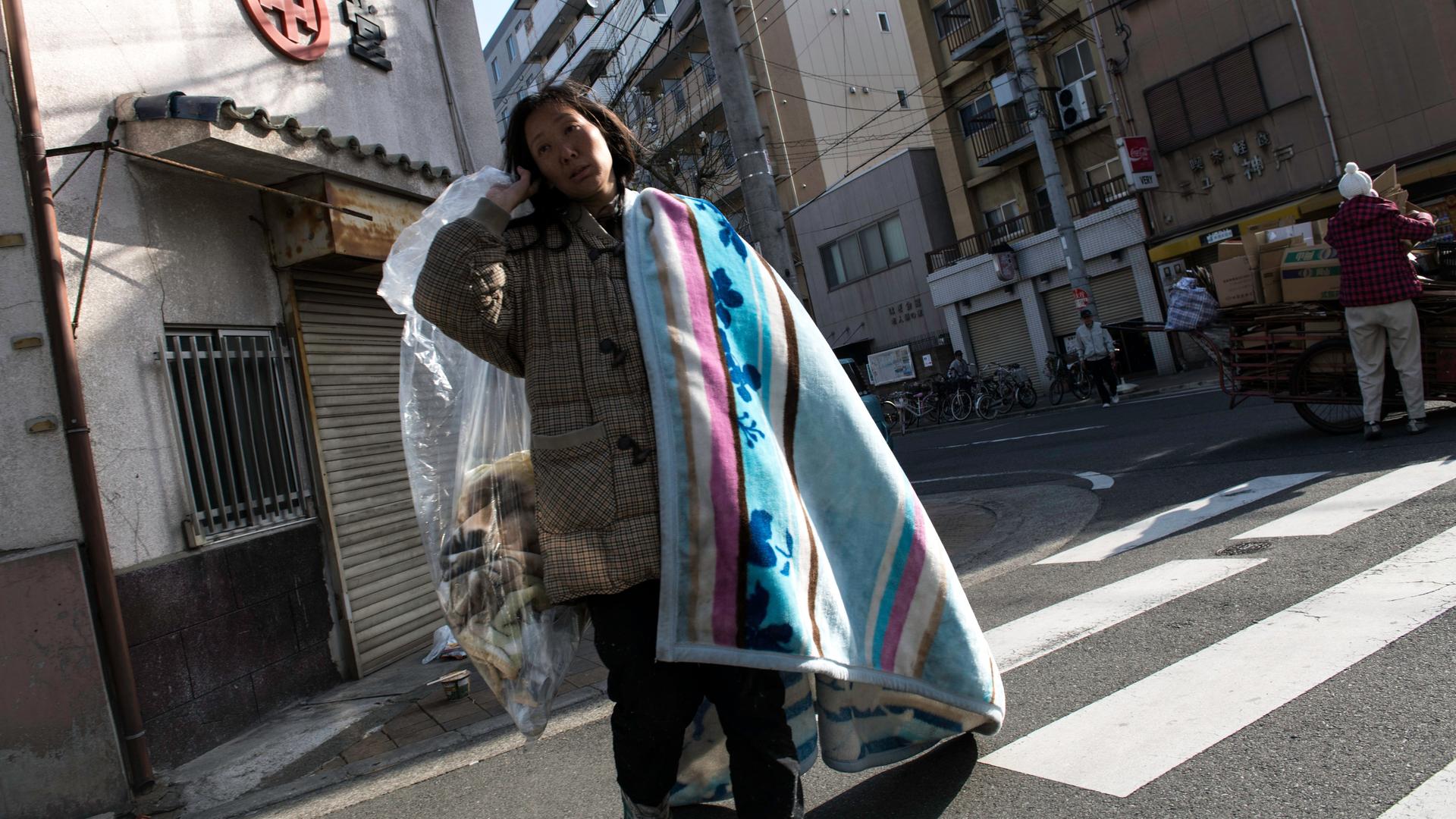 Eine obdachlose Frau geht über eine Straße mit ihrer Decke und ihren wenigen Habseligkeiten.