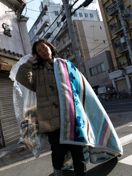 Eine obdachlose Frau geht über eine Straße mit ihrer Decke und ihren wenigen Habseligkeiten.