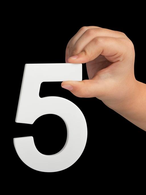 Eine kindliche Hand hält mit spitzen Fingern eine weiße Ziffer 5 vor schwarzem Hintergrund.
