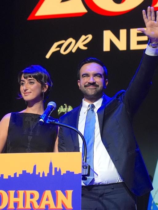 Der zum Bürgermeister von New York gewählte Zohran Mamdani steht zusammen mit seiner Frau Rama Duwaji an einem Rednerpult und spricht nach seinem historischen Sieg zu seinen Anhängern Der zum Bürgermeister von New York gewählte Zohran Mamdani steht zusammen mit seiner Frau Rama Duwaji an einem Rednerpult und spricht nach seinem historischen Sieg zu seinen Anhängern