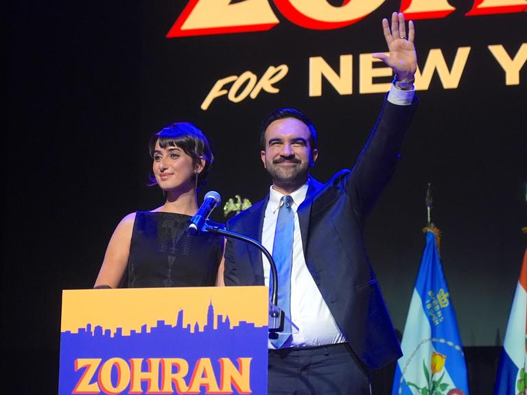 Der zum Bürgermeister von New York gewählte Zohran Mamdani steht zusammen mit seiner Frau Rama Duwaji an einem Rednerpult und spricht nach seinem historischen Sieg zu seinen Anhängern Der zum Bürgermeister von New York gewählte Zohran Mamdani steht zusammen mit seiner Frau Rama Duwaji an einem Rednerpult und spricht nach seinem historischen Sieg zu seinen Anhängern