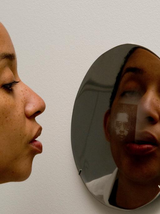 Eine Frau schaut in einen Spiegel, in dem man ihr Spiegelbild erkennt. Eine Frau schaut in einen Spiegel, in dem man ihr Spiegelbild erkennt.