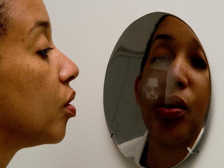 Eine Frau schaut in einen Spiegel, in dem man ihr Spiegelbild erkennt. Eine Frau schaut in einen Spiegel, in dem man ihr Spiegelbild erkennt.