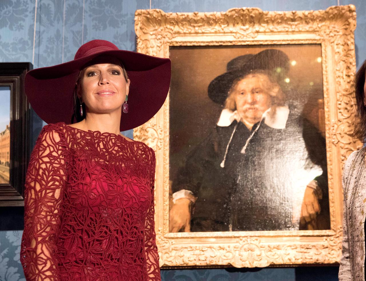 Eine Frau mit Hut und Strickkleid steht vor einem barocken Bild, das einen dicklichen Mann mit großem Kragen und Hut zeigt.