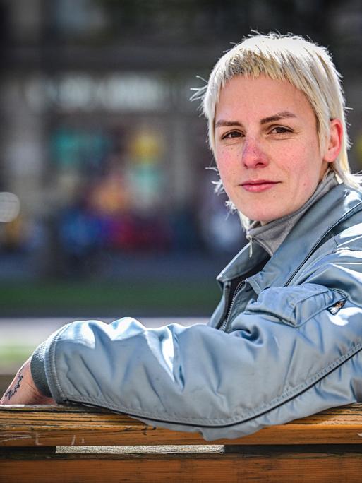Helene Bukowski sitzt auf einer Bank und schaut direkt und freundlich in die Kamera. Im Hintergrund ist eine Straße zu erkennen.