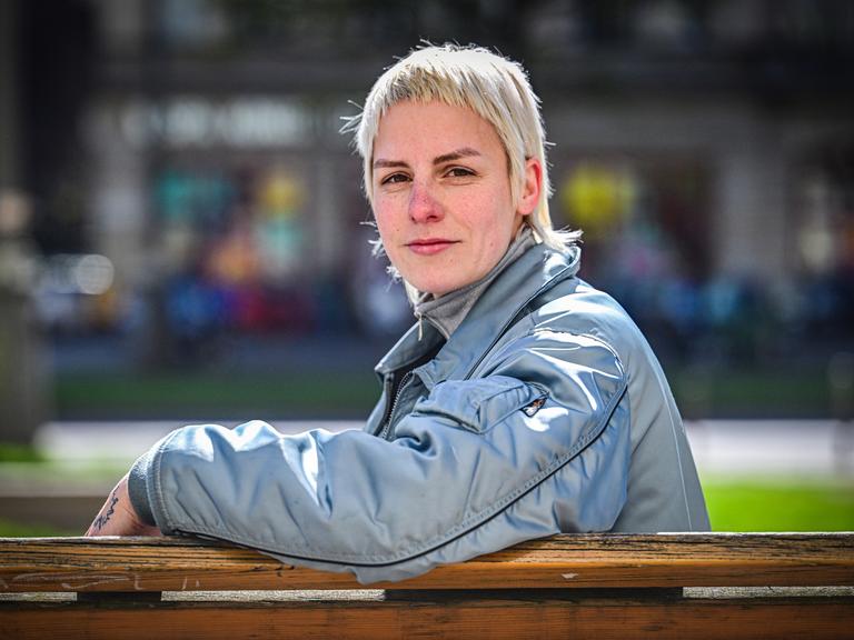 Helene Bukowski sitzt auf einer Bank und schaut direkt und freundlich in die Kamera. Im Hintergrund ist eine Straße zu erkennen.