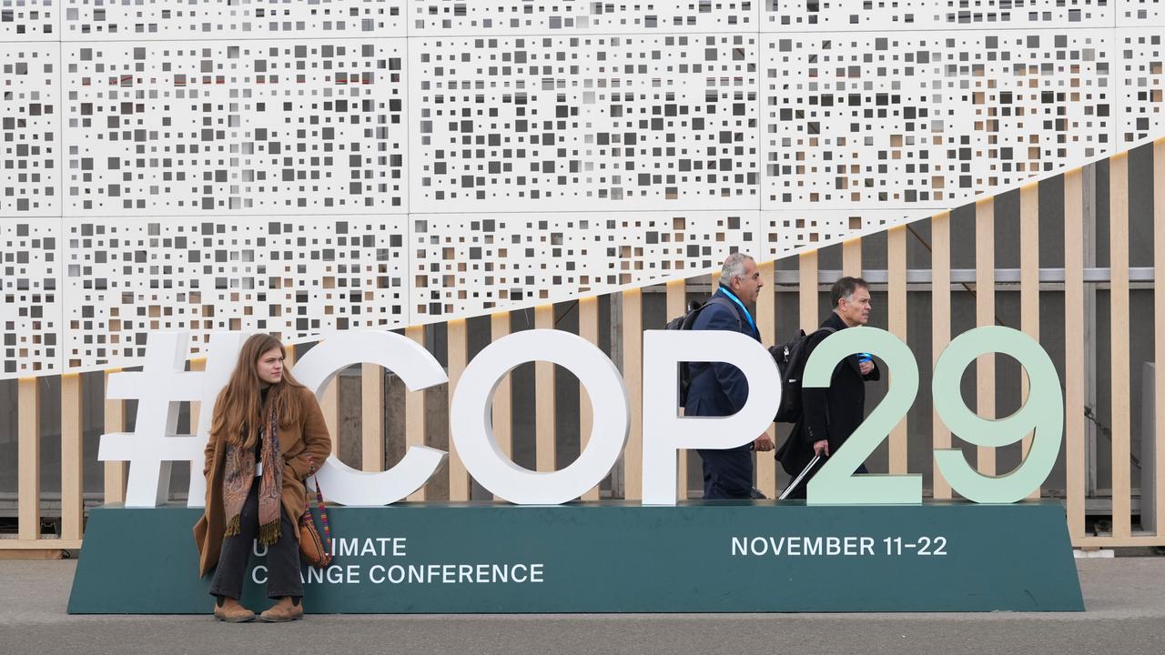 Eine Teilnehmerin sitzt vor dem Logo der COP29 in Baku. 