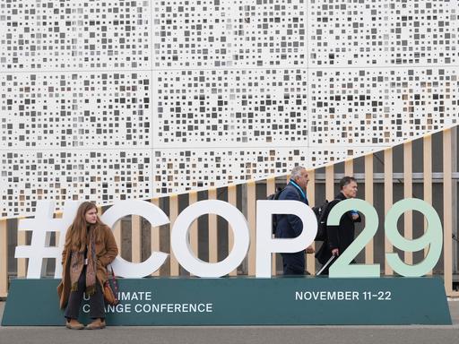 Eine Teilnehmerin sitzt vor dem Logo der COP29 in Baku. 