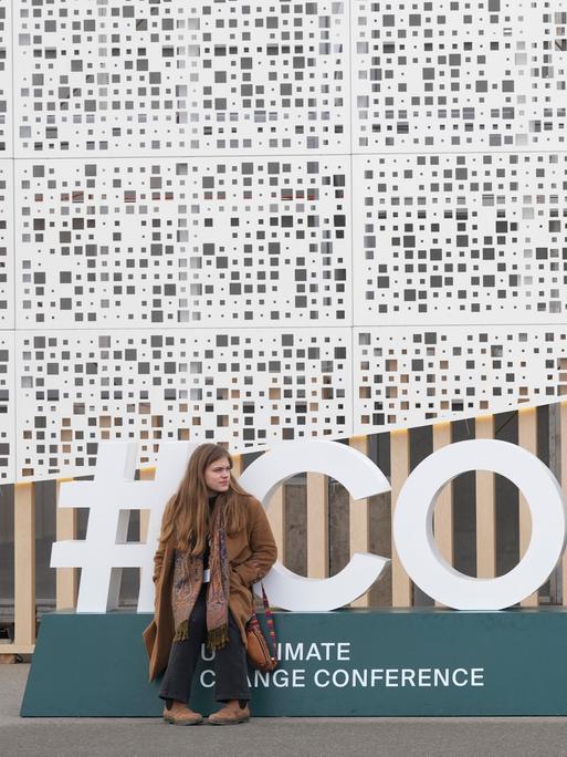 Eine Teilnehmerin sitzt vor dem Logo der COP29 in Baku. 