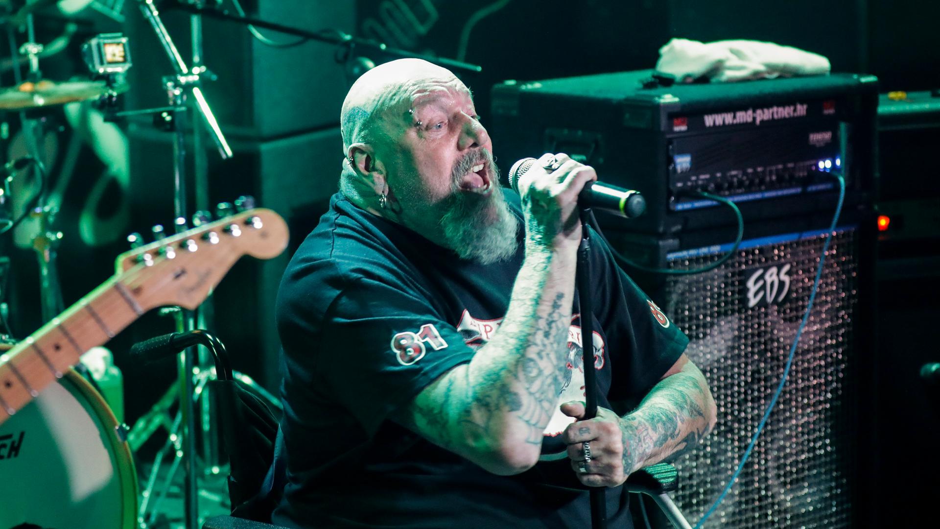 Paul Di'Anno sitzt in einem Rollstuhl auf der Bühne und singt.